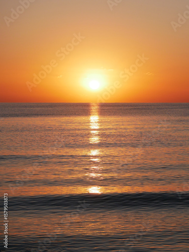Vivid sunset over the sea with a glowing sun and golden reflection on the calm water. Peaceful and captivating atmosphere. Nature background, relaxation concept, travel theme and inspirational visual