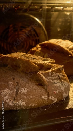 Two loaves of bread slowly rise and bake in the oven, creating a warm atmosphere filled with inviting aroma of fresh baked goods. Golden crust enhances charm. Food. Cinematic shot. Vertical video