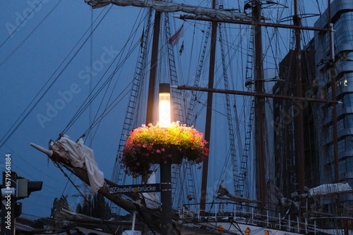 Laterne mit Blumen vor historischem Segelschiff bei Abenddämmerung im Hafen