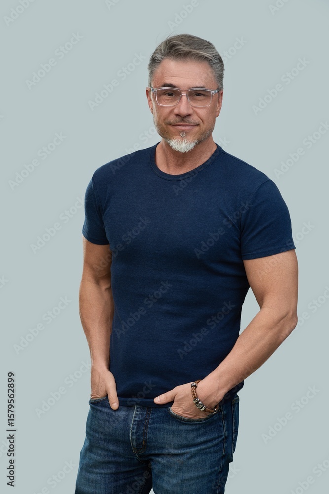 Fototapeta premium Portrait of mid adult, older, gray hair man in glasses. Male in casual and jeans standing isolated on gray background. Happy confident smile.