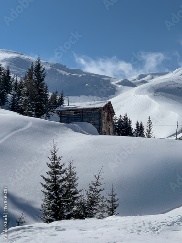 A remote mountain cabin surrounded by deep snow and majestic peaks in Georgia. Sunny winter scene in the untouched Caucasus wilderness.
