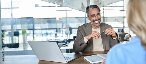 Happy middle aged professional business man executive hr or bank manager, lawyer or financial advisor having job interview or business conversation consulting client at corporate office meeting.