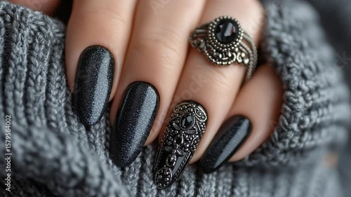 Elegant hand with long, dark glitter nails, ornate decorative nail, and ring.