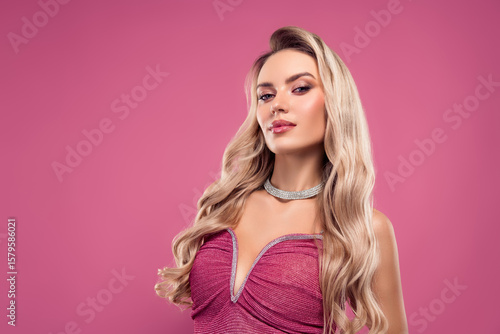 Stunning blonde woman in stylish dress posing against pink background reflecting beauty and glamour