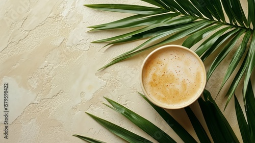 Warm Beverage Resting on Table Beside Lush Palm Leaf in Natural Light Setting.