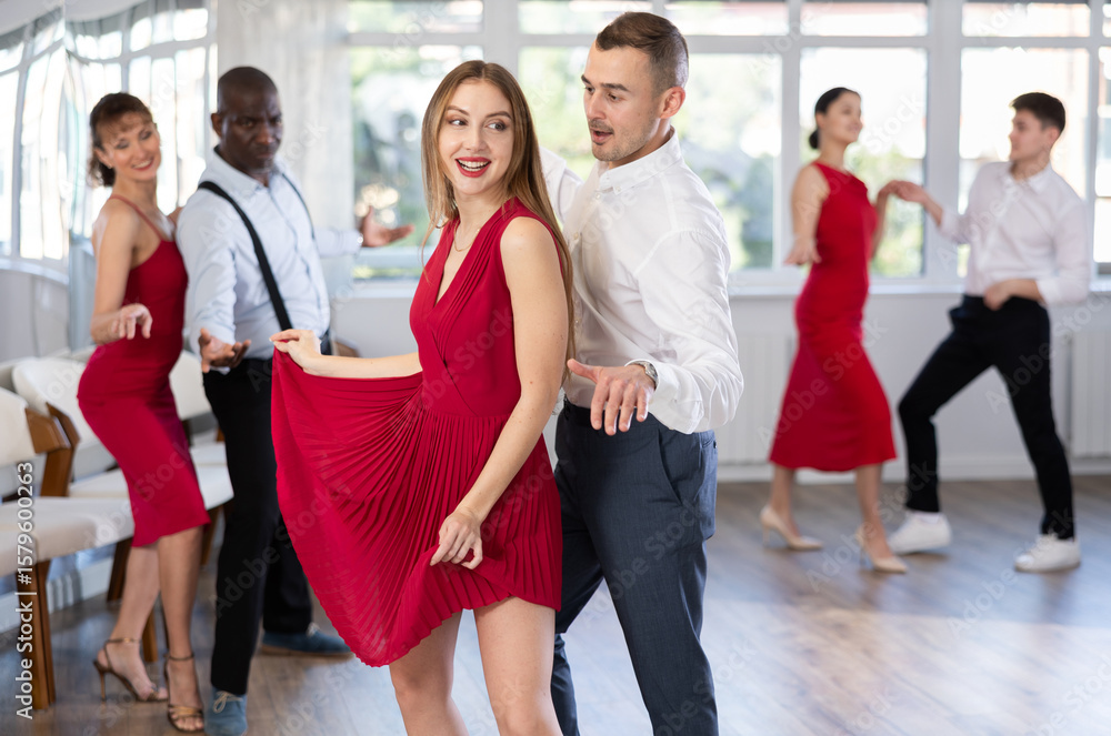 Naklejka premium Happy young Woman in red dress with man practising charleston dancing in modern dance hall