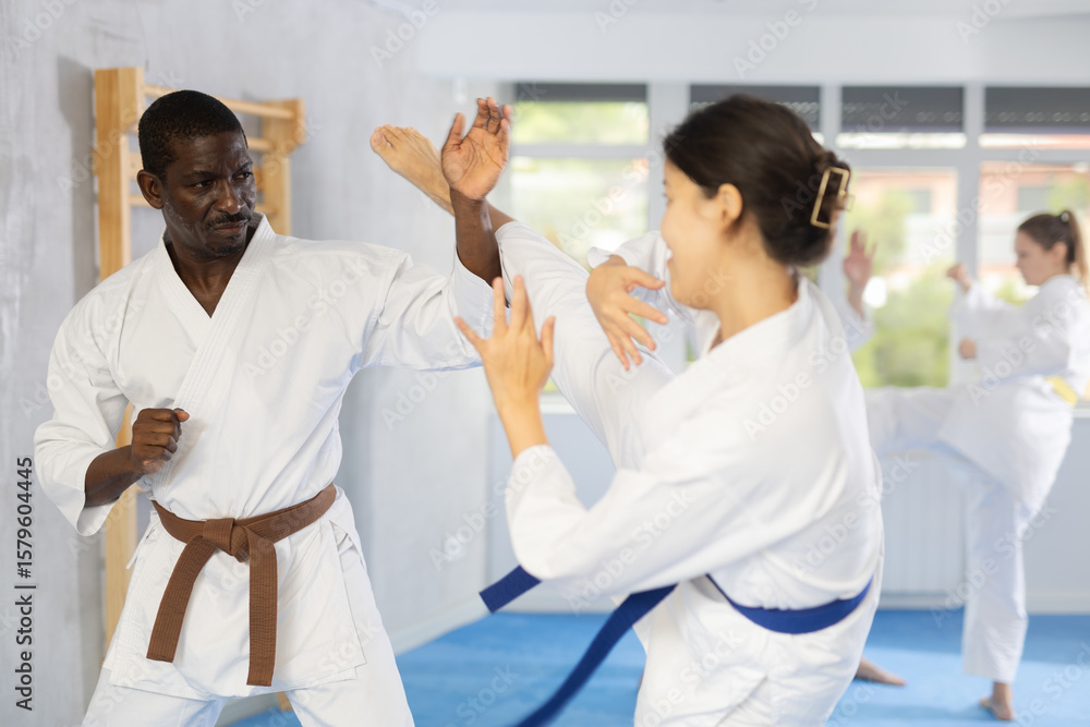 Obraz premium Adult man and young woman judokas practicing judo technique in group in gym