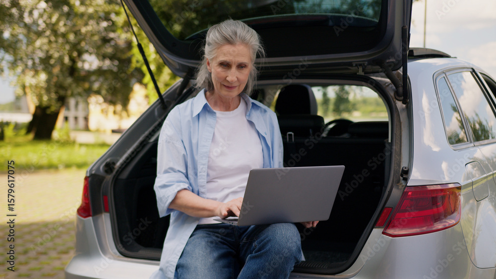 Happy smiling Caucasian elderly business woman female businesswoman aged tourist freelancer working laptop online work computer connection wifi sitting on opened automobile car trunk outdoors nature Happy smiling Caucasian elderly business woman female businesswoman aged tourist freelancer working laptop online work computer connection wifi sitting on opened automobile car trunk outdoors nature