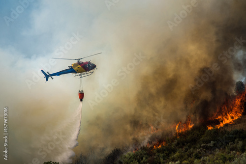Helicopter tackles forest fire in mountainous area during daytime as smoke billows into the sky