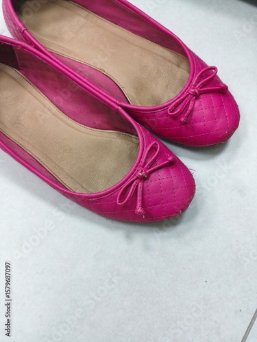 Pink quilted ballet flats with bows on white tiled floor, used women’s shoes showing signs of wear, casual feminine fashion footwear for everyday or indoor use