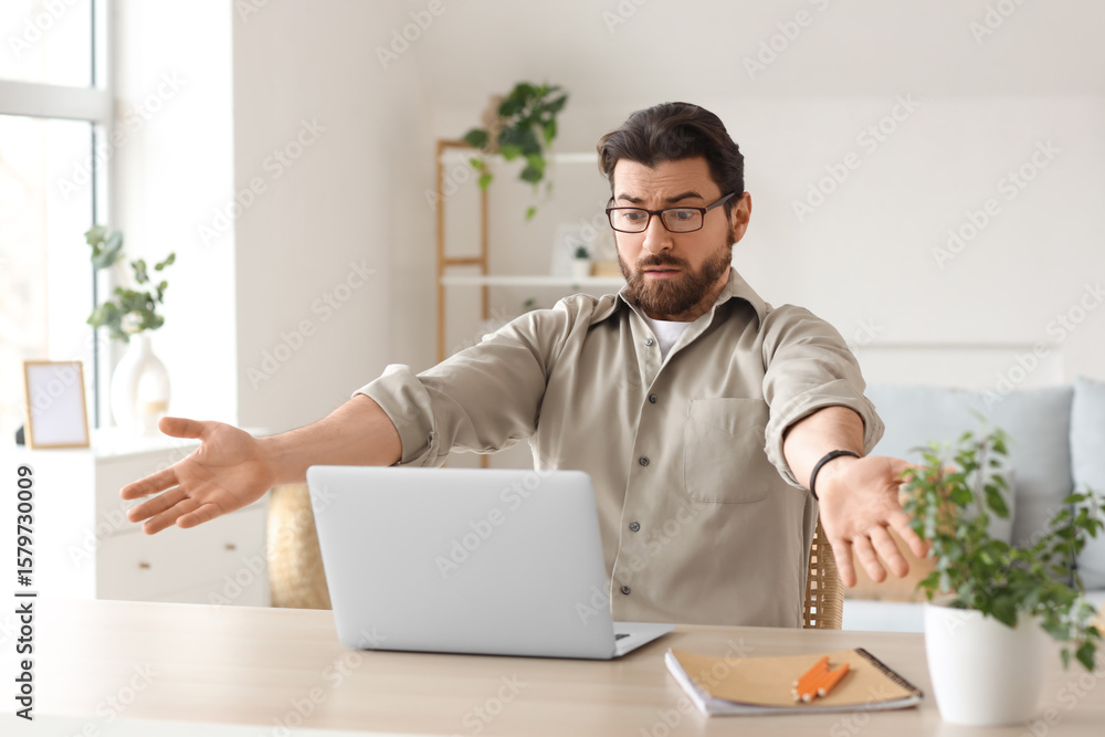 Upset fired young man with laptop on table at home Upset fired young man with laptop on table at home