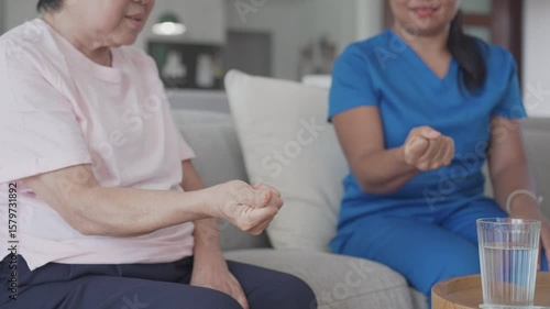 Asian health care worker giving elderly woman physiotherapy at home, home nurse, home care service concept
