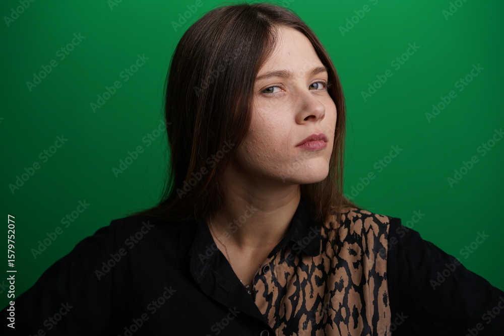 Obraz premium A young woman poses in a studio with a green background, showing natural emotions, full of expressions and dynamic movements. Unedited image