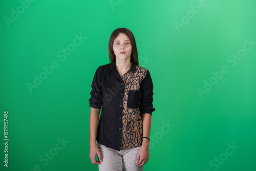 A young woman poses in a studio with a green background, showing natural emotions, full of expressions and dynamic movements. Unedited image