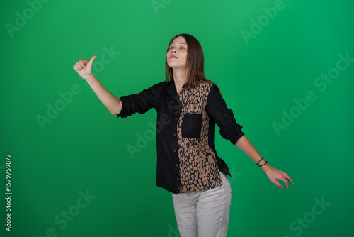 A young woman poses in a studio with a green background, showing natural emotions, full of expressions and dynamic movements. Unedited image