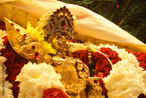 Close-Up Golden Lord Murugan Idol and Vel Decorated with Jasmine and Colorful Flowers and Peacock Feathers. South Indian Hindu Festival, Tamil Devotional Worship and Traditional Spiritual Celebration