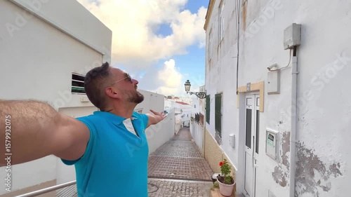 Latin american backpacker tourist taking a selfie in streets of Albufeira old town with whitewashed houses and blooming bougainvillea, a popular summer destination in the Algarve region of Portugal