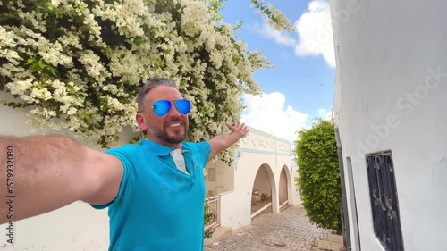 Latin american backpacker tourist taking a selfie in streets of Albufeira old town with whitewashed houses and blooming bougainvillea, a popular summer destination in the Algarve region of Portugal