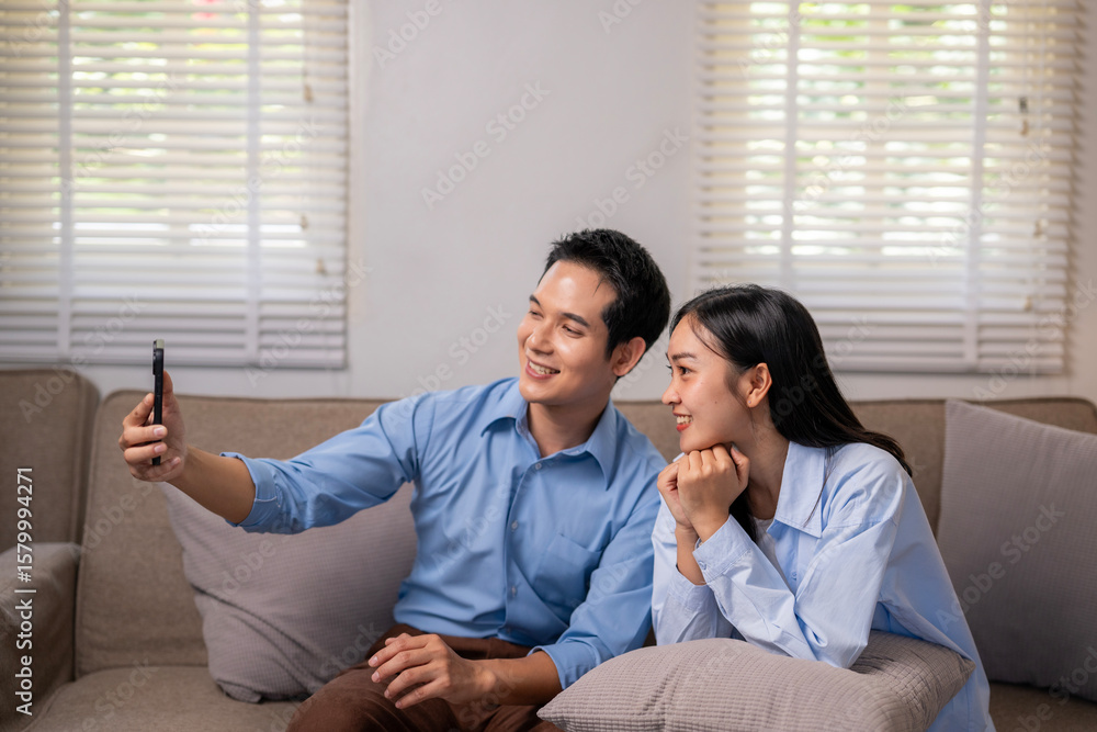 Fototapeta premium A man and woman are sitting on a couch, taking a selfie with a cell phone