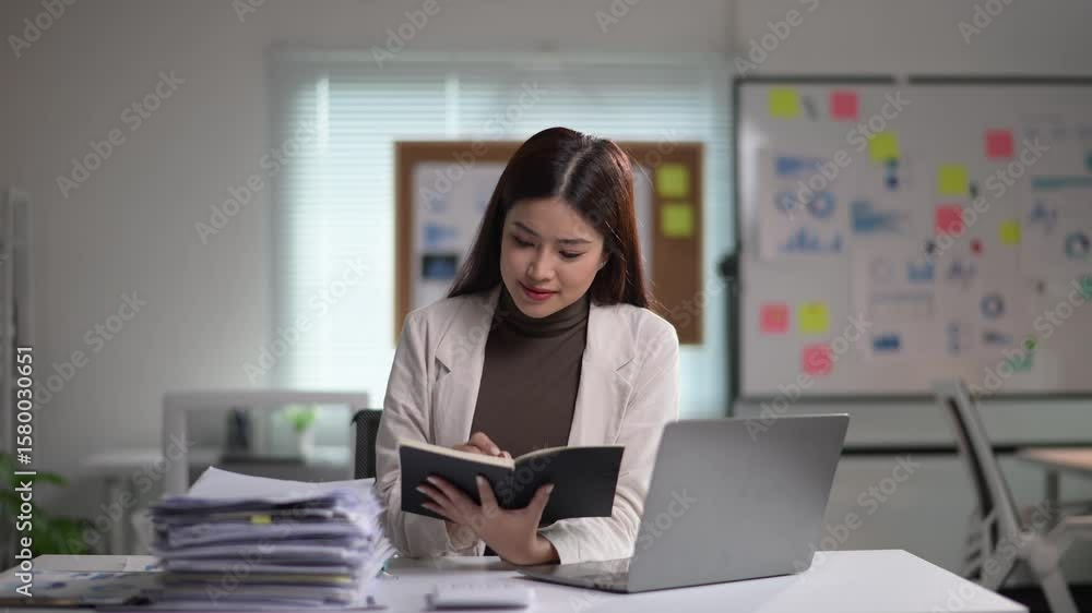 Businesswoman taking notes while working at laptop Businesswoman taking notes while working at laptop