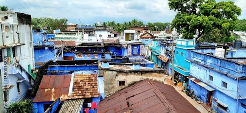 The unique charm of Indian housing, showcasing a mix of vibrant blue facades, traditional tile roofs, and corrugated metal structures in a bustling village setting under cloudy sky