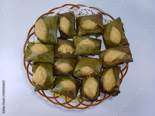 Basket filled with multiple servings of a traditional steamed or boiled snack, individually wrapped in banana leaves. Related to cultural snacks or desserts prepared with authentic natural wrappers