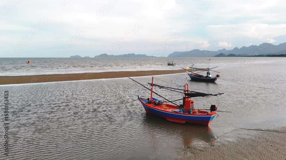 Traditional Thai fishing boats resting on sandbank at low tide with distant mountains, symbolizing local seafood trade and livelihood Traditional Thai fishing boats resting on sandbank at low tide with distant mountains, symbolizing local seafood trade and livelihood