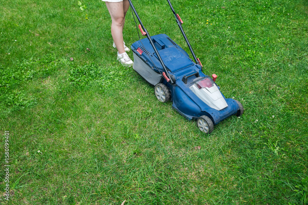 This image captures someone mowing their lawn with a push lawn mower. The person is holding onto the handle, guiding the mower over a well-maintained grassy area. This image captures someone mowing their lawn with a push lawn mower. The person is holding onto the handle, guiding the mower over a well-maintained grassy area.
