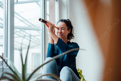Woman looking through antique monocular sitting by window