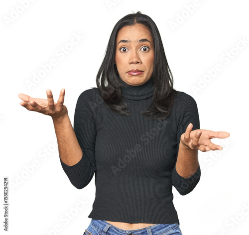 Simple portrait of a young Latina doubting and shrugging shoulders in questioning gesture.