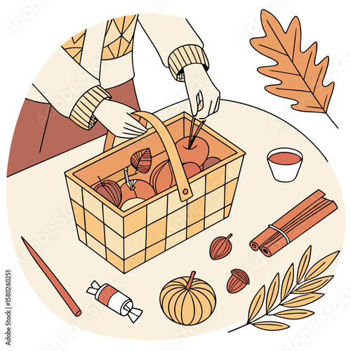 A person wearing a cozy sweater is arranging apples in a woven basket surrounded by autumn elements like leaves a pumpkin cinnamon sticks and a cup of drink