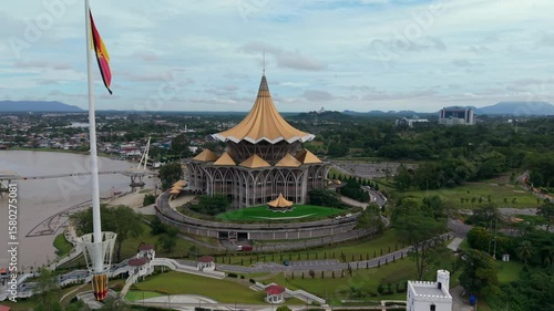 Aerial view of the sarawak state legislative assembly building with golden dome roof and modern pedestrian darul hana bridge crossing the sarawak river