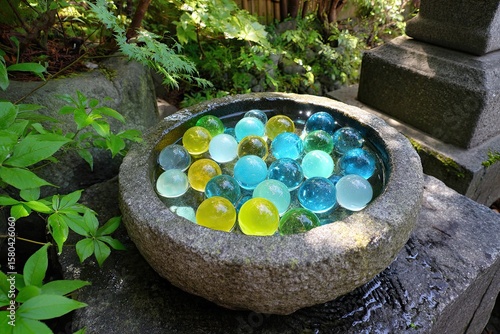 Colorful glass orbs in a stone basin, nestled amidst greenery