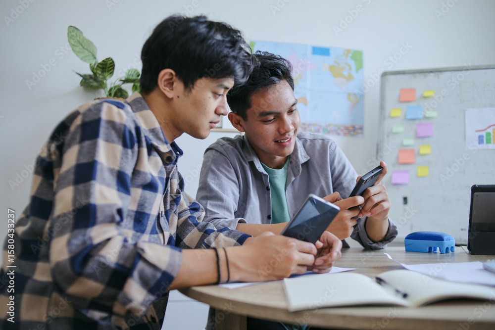 Obraz premium Two Young Men Intently Focused On Their Smartphone Sharing Moment