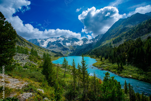 Landscape lake with snow capped mountains and lush greenery under blue sky
