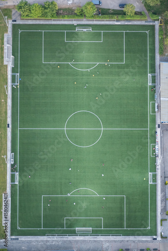 football soccer field pitch with game match in progress shot from hot air balloon above for birds eye view of players. green flat plan with white line markings