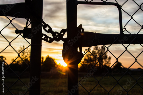 Morning sun shining through silhouetted padlock and gates