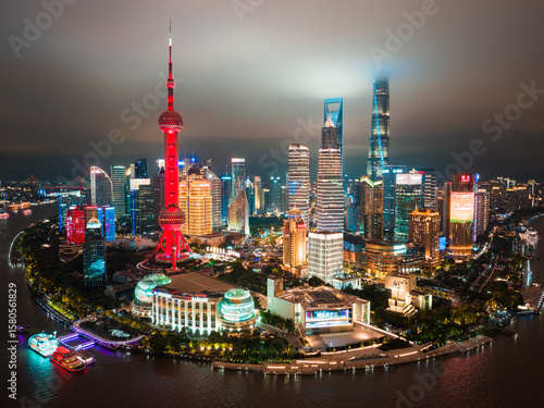 Shanghai, China - 21 June 2025: Aerial view of The Bund's luminous skyline, where the Oriental Pearl Tower glows red against the dark sky, reflecting on the river.