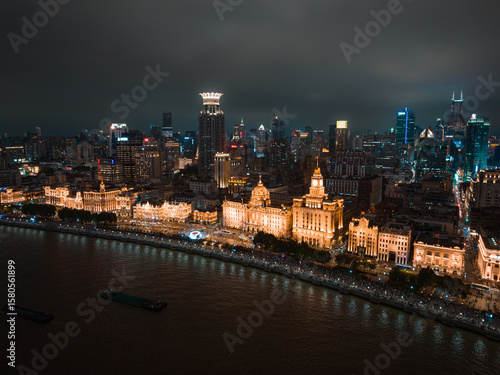 Shanghai, China - 21 June 2025: Aerial view of Shanghai's glowing Bund and Pudong skyline shimmer over the dark Huangpu River, a symphony of light and shadow.