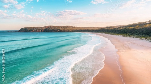 Serene coastal view.  Gentle waves lap a pristine beach, framed by lush green hills and a vibrant blue ocean