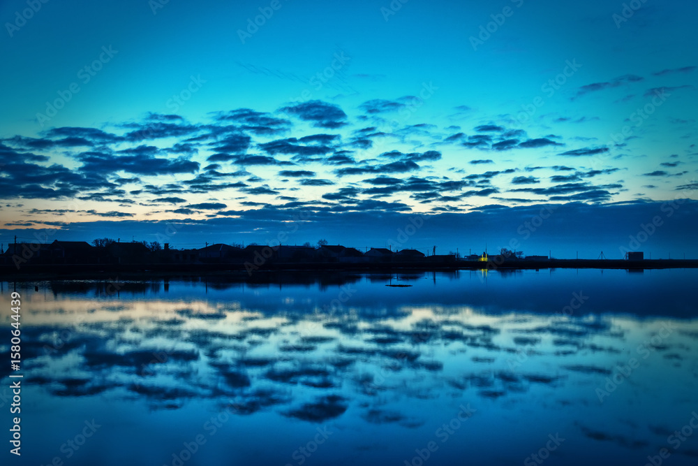 Fototapeta premium Piscatory settlement, fishing village on the shore of a quiet lagoon. Dawn, clouds, and vague reflections