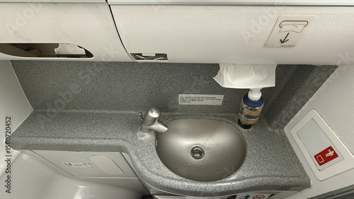 Compact Airplane Lavatory Sink Area with Soap Dispenser, Towel, and Signage for Passengers