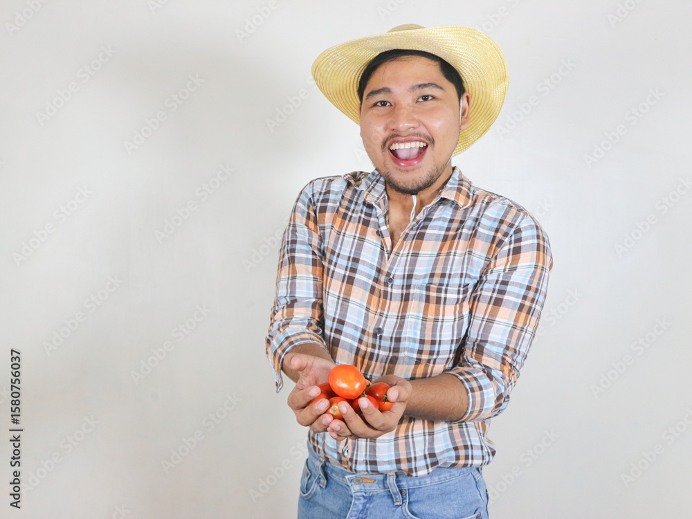 Fototapeta premium Asian male farmer wearing a rattan hat showing the tomatoes he has harvested, with an excited expression