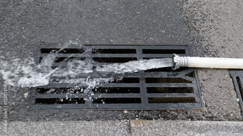 Water pouring from a fire hose in an endless stream and flowing into the sewer. Careless and inept waste of water. A blow to the green ecology of our planet.