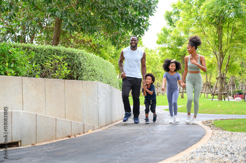 Happy African American family in sportswear running in public park. father carrying son with mother and daughter. Family exercising together concept.