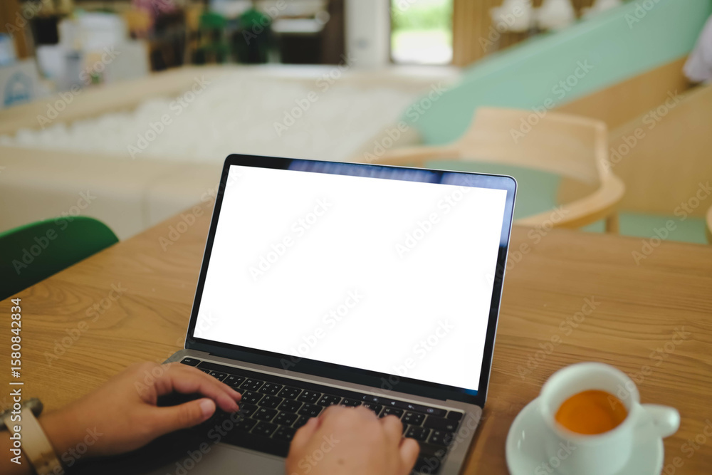 Fototapeta premium A person works on a laptop with a blank white screen in a kids' cafe or play area, illustrating remote work and family lifestyle.