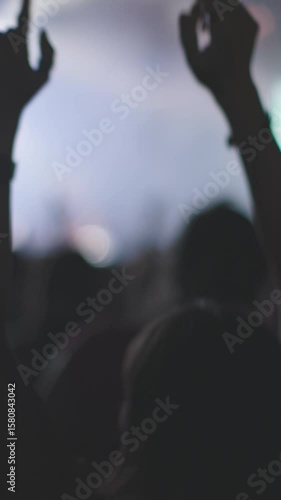 vertical shot. Girls enjoy rock show with raised hands, flashing lights and powerful atmosphere. Audience enjoys live music concert with bright lights and energetic atmosphere.