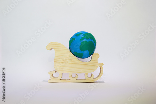 Miniature Earth globe positioned on wooden Christmas sleigh against white background, symbolizing global holiday celebration and environmental awareness. Sustainable christmas. Eco-friendly christmas 