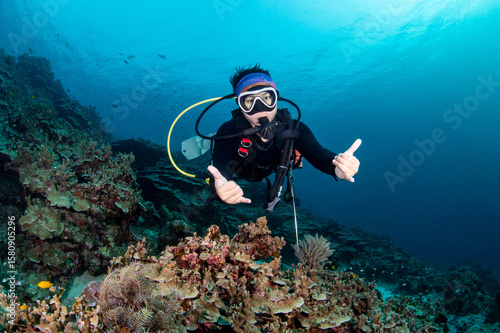 Asian female scuba diver diving looking at camera in Andaman sea, Thailand. Recreational underwater activity to explore marine life.