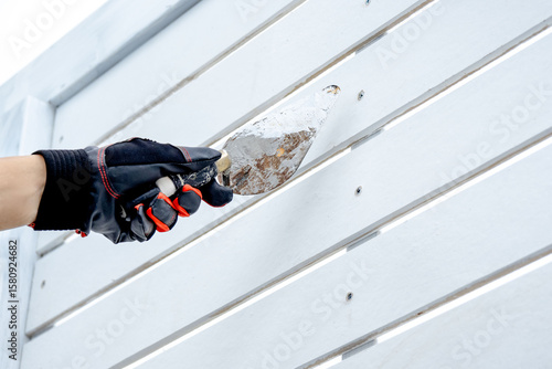 Fotografie Male construction worker hand in protective glove using plastering trowel for bolt head grouting on white wooden wall panel